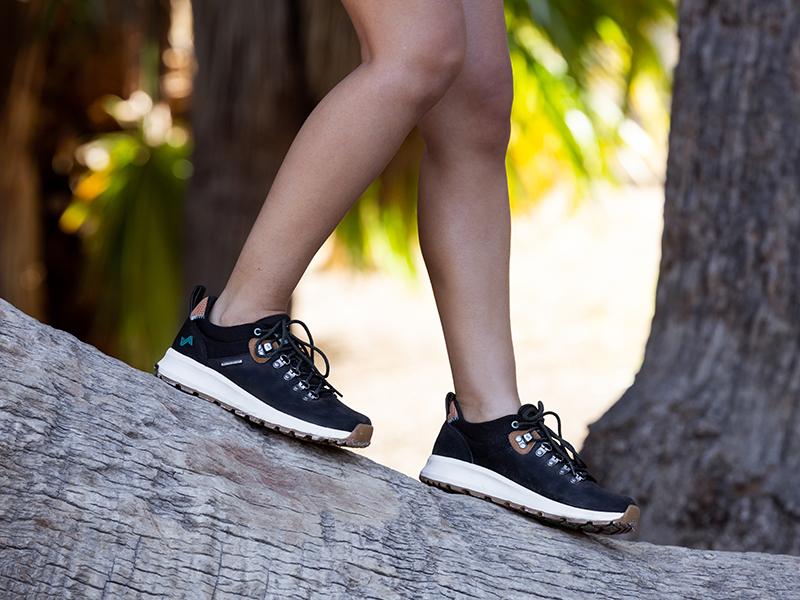 The image features a person wearing the Thatcher Low Waterproof Women's Trail Shoes in Black/Tan.