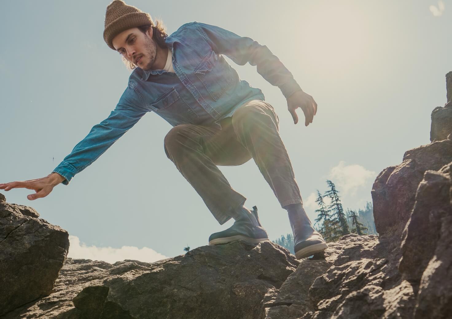Shop All Forsake Men's Shoes featuring a man wearing the Phil Chelsea Waterproof Outdoor Sneaker Boot in Black on a rocky terrain.